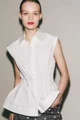 Camisa blanca de cuello solapa y sin mangas, con bajo acabado en peplum y cierre frontal con botones ocultos.