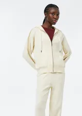 Campera de punto con cierre frontal, capucha con cordones ajustables y bolsillos tipo canguro. Presenta un diseño de manga larga con detalles acanalados en los laterales y puños.