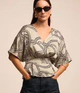 Blusa de tela satinada color gris con estampado abstracto en negro y blanco, escote en V cruzado, mangas cortas y cintura elastizada.
