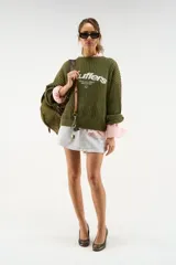 Jersey oversized de punto en color verde caqui, con cuello redondo, mangas largas y puños ajustados. Presenta el logotipo de la marca bordado en el pecho en color blanco.