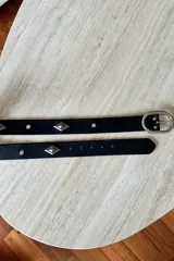 Cinturón de cuero vacuno color negro con apliques metálicos en forma de rombo y hebilla ovalada plateada.