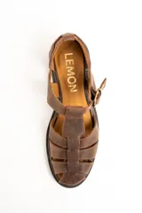 Sandalias tipo cangrejera de cuero color marrón, con diseño de tiras cruzadas, talón cerrado y tira ajustable con hebilla metálica y detalle de estrella grabada en el lateral. Suela plana con pequeño tacón.