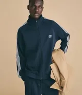 Campera deportiva de cuello alto con cierre frontal completo, mangas largas con rayas laterales blancas contrastantes y bolsillos laterales. Presenta un bordado pequeño en el pecho.