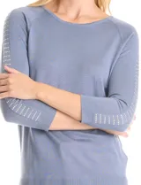Buzo de tejido fino en color blanco, con cuello redondo y mangas raglán tres cuartos. Presenta una línea de tachas decorativas a lo largo de las mangas.