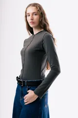 Camiseta de manga larga en color gris oscuro, con cuello redondo y costuras decorativas expuestas en el frente. Presenta un diseño ajustado al cuerpo.