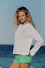 Remera blanca de manga larga y cuello redondo con detalle de texto impreso en el pecho en color azul.