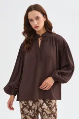 Blusa de lyocell color marrón, con diseño holgado, escote en V con cordón para atar y mangas largas abullonadas con puños ajustados.
