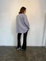 Camisa a rayas verticales azules y blancas, de popelina de algodón, con cuello verde y botones marmolados a tono. Es corta adelante y larga atrás.