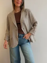 Blazer de lino color beige, de corte relajado y líneas clásicas. Presenta cuello con solapas, cierre frontal con dos botones y bolsillos con solapa en el frente.