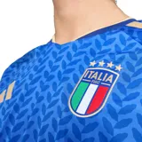 Camiseta de fútbol Adidas de la selección italiana, modelo Local 26, color azul con patrón de hojas repetidas en tono más oscuro. Presenta cuello en V con ribete dorado y detalles dorados en los hombros y puños. Escudo de la FIGC y logo de Adidas en dorado en el pecho.