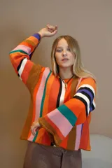 Sweater de algodón tejido a rayas verticales en el cuerpo y horizontales en las mangas. Presenta una mezcla de colores vibrantes como naranja, rosa, verde azulado, marrón, blanco, negro y violeta. Tiene terminaciones en crochet en los puños.