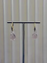 Aros tipo argolla dorada con dije colgante de vidrio soplado en forma de lágrima estriada de color rosado traslúcido.
