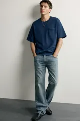 Jeans flare fit de denim rígido en color azul con efecto lavado. Presentan tiro medio, diseño de cinco bolsillos y cierre frontal con cremallera y botón.