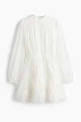 Vestido corto de color blanco, confeccionado en mezcla de lyocell, con cuello mao de volados, mangas globo largas y falda con fruncido escalonado e inserciones de encaje en escalera.