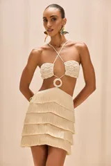 Vestido corto de crochet color beige, con busto de crochet y tirantes cruzados. Presenta una hebilla con ribete de crochet en la cintura y una falda con flecos en capas. Cierre con cremallera invisible en la espalda.