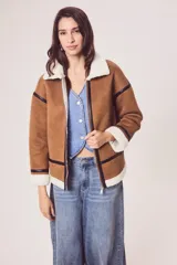 Campera marrón de gamuza sintética con cuello, puños y ruedo de piel sintética blanca. Presenta cierre frontal con cremallera, bolsillos laterales y detalles en cuero sintético negro.