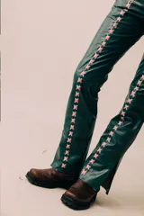 Pantalón de cuero de tiro medio y silueta recta levemente acampanada, color azul marino, con cierre frontal y recortes laterales intervenidos con pasacintas entrelazadas en contraste.
