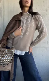 Sweater de punto color beige con bordado de flores blancas en el frente y las mangas, cuello redondo y puños acanalados.