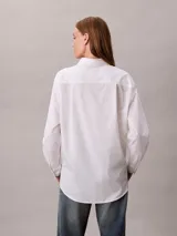 Camisa blanca de algodón con cuello camisero, manga larga y cierre frontal con botones. Presenta un sutil estampado integral de logo de Calvin Klein.