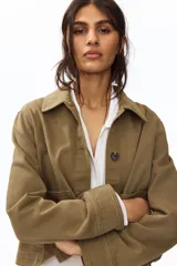 Campera camisera corta de sarga de algodón color verde militar, con cuello camisero, cierre frontal de botones oscuros y dos amplios bolsillos delanteros de parche.