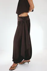 Pantalón de tiro alto color bordó con leve brillo, cintura cruzada con detalle de lazo lateral y piernas estilo globo con elásticos en los tobillos.