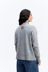 Sweater de tejido de punto color marrón con diseño estampado de flores en tonos rosados. Presenta cuello alto, mangas largas con puños ajustados y un corte relajado con terminación recta en la cintura.