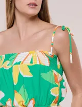 Top crop de rayón con estampado floral tropical en tonos verdes, amarillos y blancos. Presenta escote recto, frunces elastizados en el pecho y la cintura, y tirantes finos para anudar en los hombros.