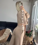 Conjunto color beige compuesto por un top corto con escote en V, botones frontales y mangas largas abullonadas con puños elásticos, y un pantalón de tiro alto con lazo en la cintura.