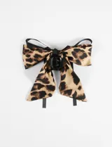 Broche para el pelo con forma de moña con lazo de tela con estampado animal print y pinza de plástico negra.