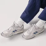 Championes New Balance modelo 204L, de estilo running retro con diseño multicapa. Presentan una combinación de tonos grises en la capellada de gamuza y malla, con el logo N en azul oscuro y detalles en el talón. La suela es de EVA con diseño inspirado en los años 2000.