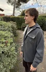 Camisa gris de lana con capucha, cierre frontal con botones a presión, manga larga y bolsillo de parche en el pecho izquierdo con logo bordado.