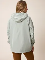 Campera de corte recto y estilo funcional, color beige, con capucha integrada, cierre frontal con botones a presión y bolsillos delanteros amplios. Presenta un diseño minimalista con cordones ajustables en la capucha.