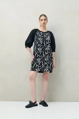 Vestido corto negro con bordado floral blanco, escote redondo con abotonadura frontal y mangas 3/4 abullonadas con pliegues en los hombros.