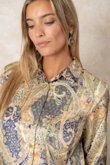 Camisa de satén con estampado paisley en tonos azules, mostaza y beige. Presenta cuello clásico, cierre frontal con botones dorados y puños anchos.