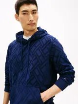 Buzo con capucha de Tommy Hilfiger, color azul marino, con patrón jacquard geométrico en relieve, bolsillo frontal tipo canguro y cordones ajustables en el cuello. Cuenta con puños y dobladillo acanalados, y detalle de la bandera bordada en el puño.