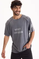 Remera gris de manga corta con lavado acid wash y diseño raglán con vivos en contraste. Presenta estampa frontal con el texto "WEST DIVISION" y número en la manga.