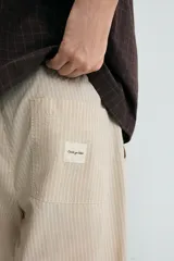 Pantalón relaxed fit color beige con rayas verticales finas, confeccionado en tejido de algodón. Cuenta con cintura elástica ajustable con cordón, bolsillos frontales y bolsillos traseros de plastrón.
