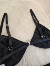 Conjunto de bikini negro con apliques de tachas cuadradas plateadas. El corpiño es de estilo triangular con una argolla central metálica y breteles regulables. La bombacha es de corte colaless con tiras laterales ajustables y argollas metálicas en los extremos.
