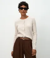 Cardigan de punto canelado en color beige, con cuello redondo, manga larga y cierre frontal con botones. Presenta un diseño ajustado al cuerpo.