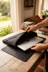 Funda para laptop de cuero natural color negro, con cierre principal y bolsillo exterior con cierre metálico.
