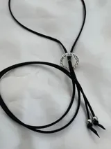Choker de cinta negra con dije circular central decorado con cristales y tiras colgantes.