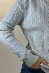 Buzo de hilo de punto con diseño de trenzas verticales, cuello alto y cadena metálica decorativa incorporada en la parte frontal.