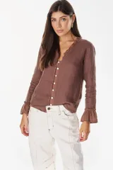 Blusa de lino color marrón, de manga larga, con escote en V y detalles de volados en el cuello y en los puños. Cuenta con cierre frontal de botones de nácar.