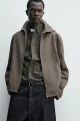 Sobrecamisa relaxed fit de Zara confeccionada en tejido negro con estructura diagonal. Presenta cuello subido, manga larga, bolsillos de vivo en la cadera y cierre frontal con cremallera.