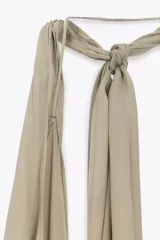 Vestido largo color beige topo, con escote halter y profundo escote pico pronunciado. Presenta un diseño drapeado con volumen en la zona del busto y espalda descubierta.