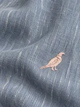 Camisa de lino color blanco, manga larga, con cuello corto clásico y bordado de un ave oscura en el pecho.