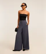 Pantalón de vestir ancho tipo pantalona, color azul grisáceo, con talle alto y pliegues frontales. Incluye un cinturón fino del mismo tejido con hebilla metálica rectangular dorada.