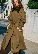 Trench coat de algodón en color verde oliva, con diseño largo y oversize. Presenta cuello camisero de pana, cierre de doble botonadura, cinturón con hebilla, trabillas en hombros y puños ajustables.