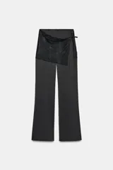 Pantalón largo de satén negro con pareo de encaje superpuesto en la cintura y lazada lateral. Cierre lateral con cremallera oculta.