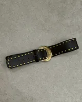 Cinturón negro de cuero sintético con hebilla metálica dorada envejecida y tachas doradas.